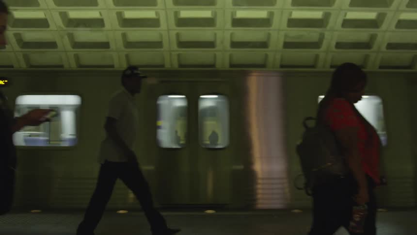 People walk by a moving train in a station