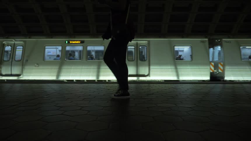 A subway train is moving and people are walking outside