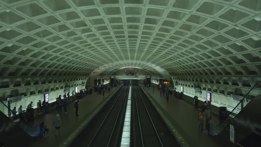 A large train station with escalators in the middle and people walking on either side