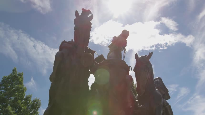 A bronze statue of three horses stands tall under sunny skies