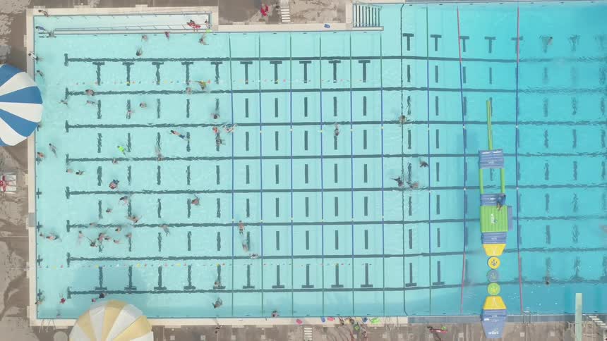 Camera looks down on a swimming pool with people swimming