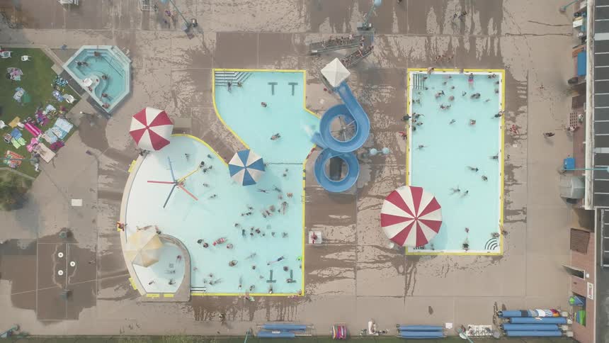 A person rides down a water slide into one of the pools were several people are swimming