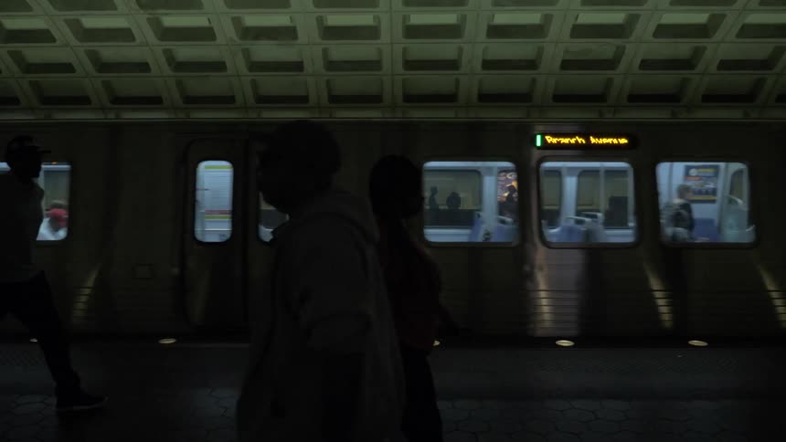A train pulls into a station with many walking nearby