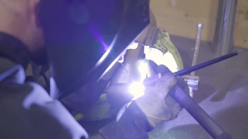 A man welds two pieces of metal together with the help of a vice
