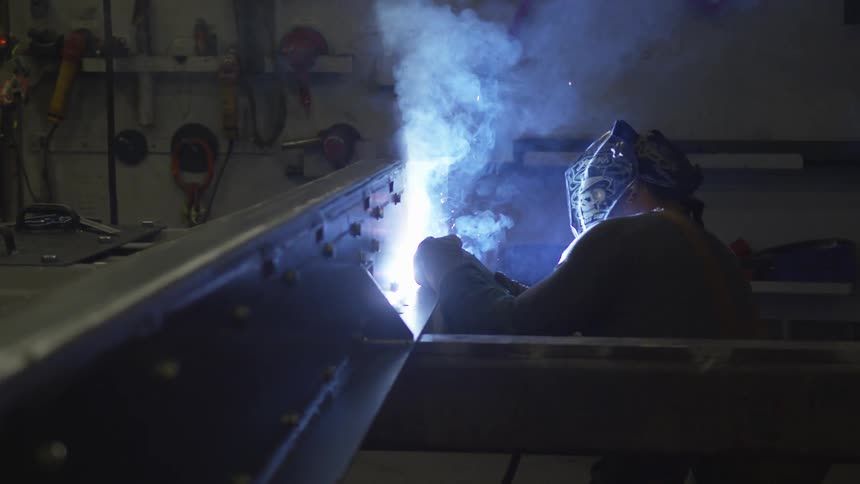 A person welding metal indoors with a torch and welding helmet