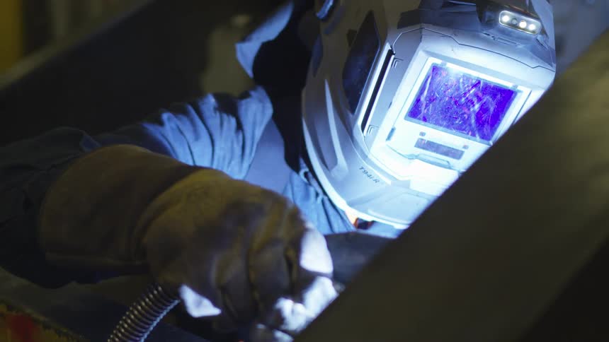 A person in a welding suit and helmet welding on metal