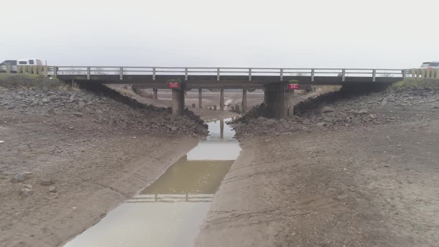 A stream of muddy water running under a car bridge
