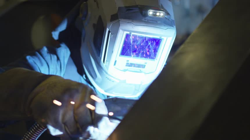 A person wearing a welding hood and holding a welding rod with gloved hands is welding something