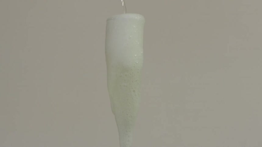 Champagne is poured into a champagne flute until bubbles overflow from the glass