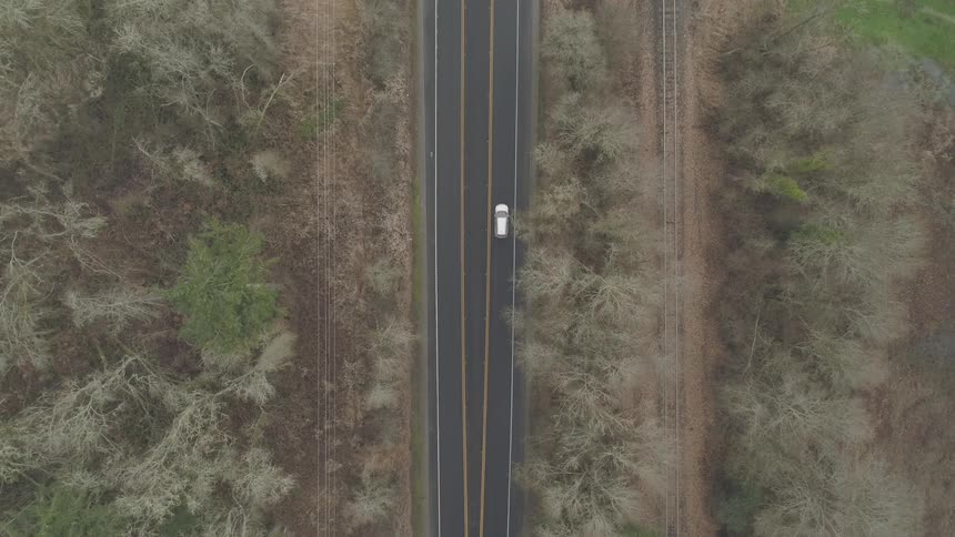 White car drives down on road with yellow lane by day