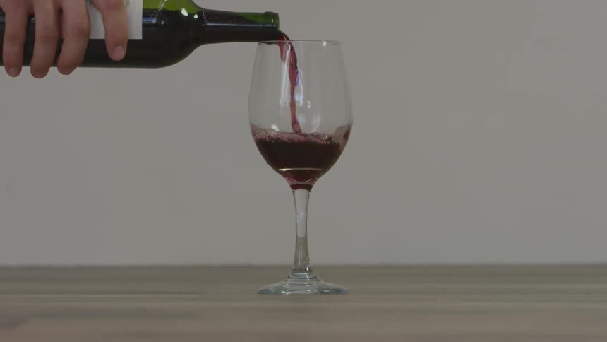 Man pours wine from wine bottle into glass by day