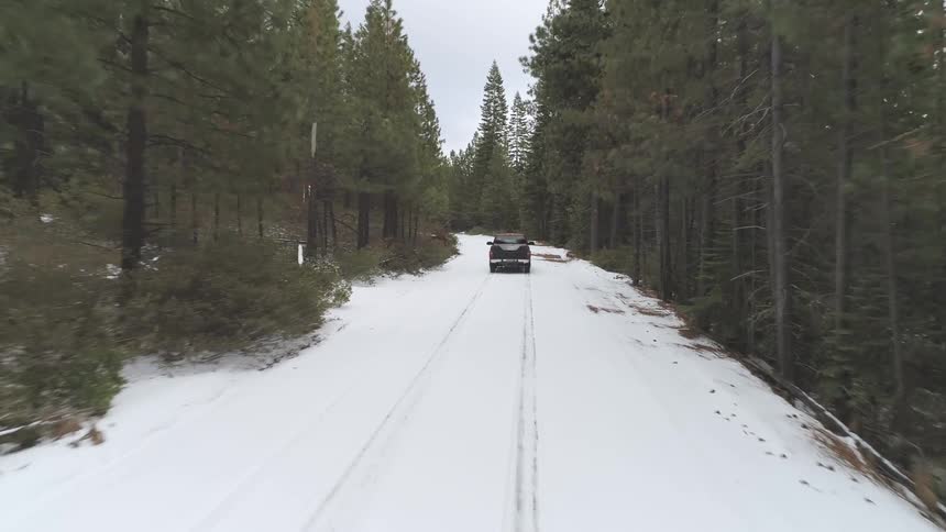A pickup truck travels along a snow covered road through a forest