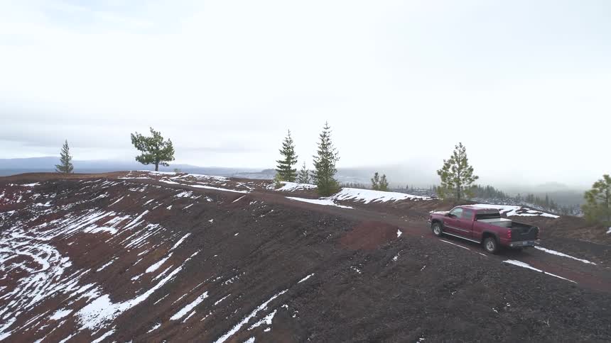 A pickup truck driving on a dirt road with the sky and trees in the background