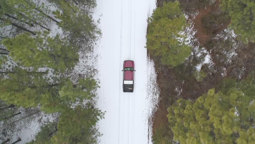 A red car drives through the forest on a snowy road