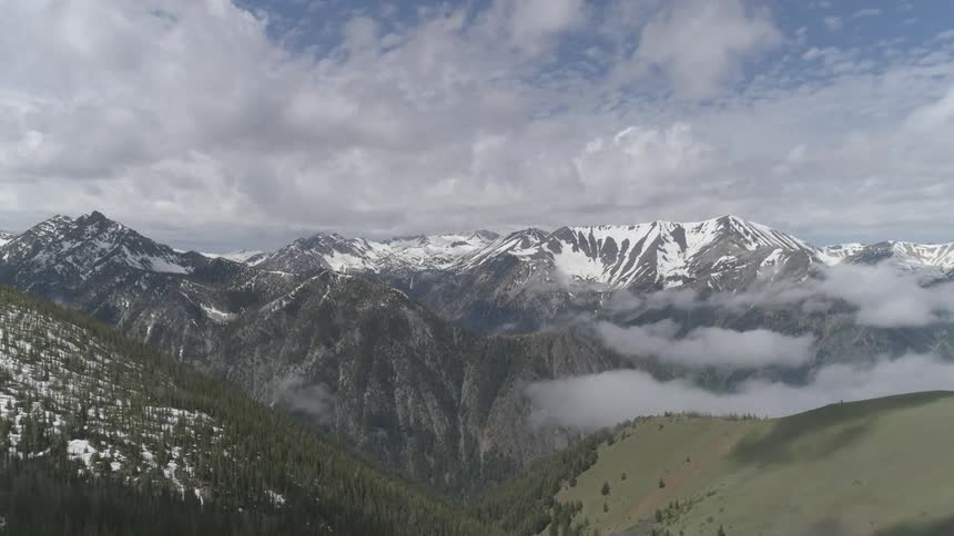 Snow covered mountains sit under the cloudy blue sky