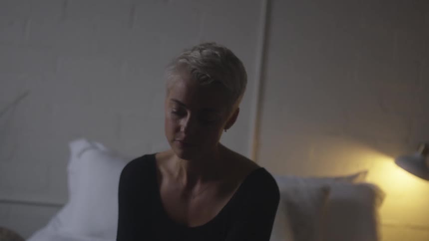 A young blonde woman sits on a bed and cries