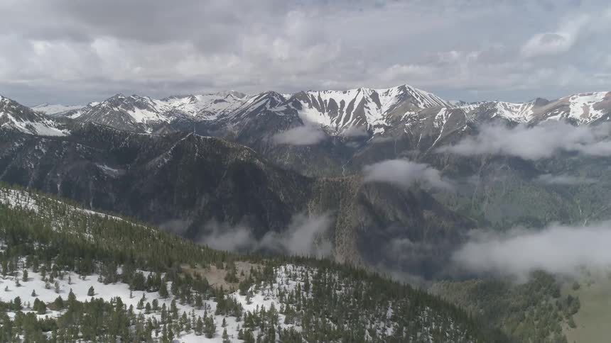 A huge sloping hill covered in snow and sparse trees leads down to the base of a mountain range