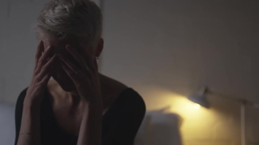 A woman with short blonde hair cries with her head in her hands
