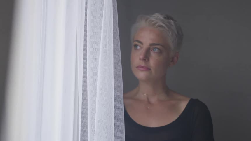 A woman standing by a woman and looking through the sheer curtains