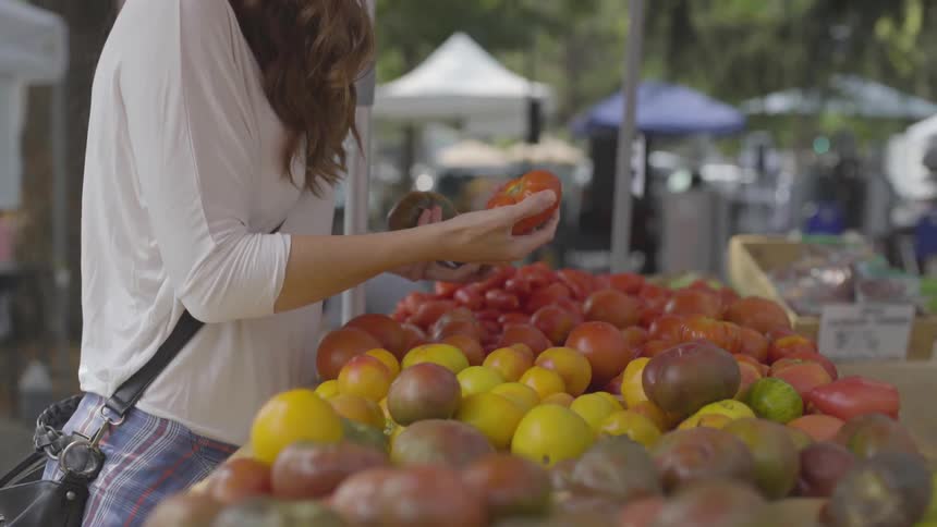 A woman comparing tomatoes at a farmers market