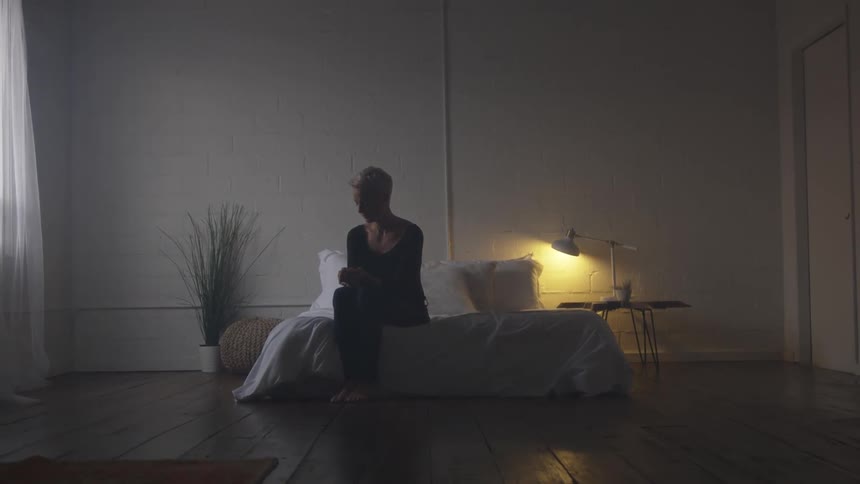 A short haired blonde woman sitting on a low bed during the day