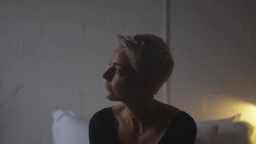 A young blonde woman sits on a bed and cries