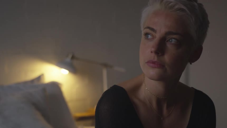 A woman sits on a bed in a dimly lit room