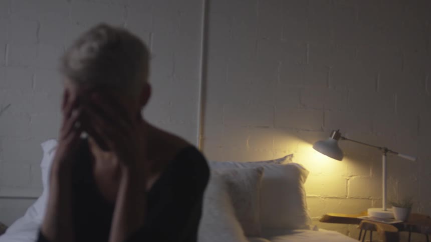 A woman sitting on the edge of a bed with her hands over her face