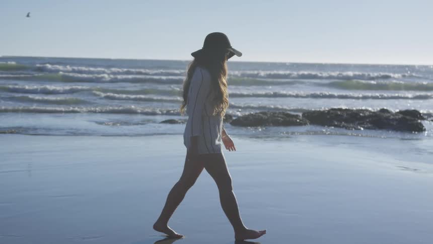 A woman walking on the beach in a sun hat