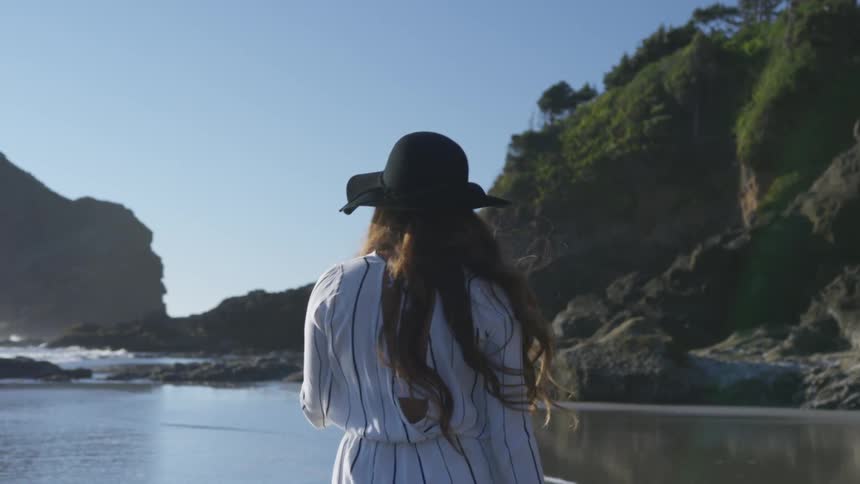 Woman in a hat walking on the beach near a cliff