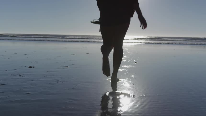 Woman skips along beach toward ocean