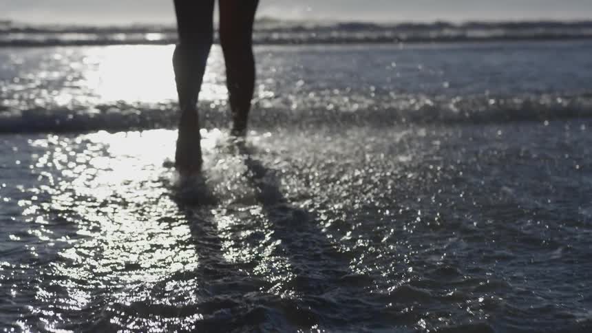 A woman runs towards the sea as shallow waters splash