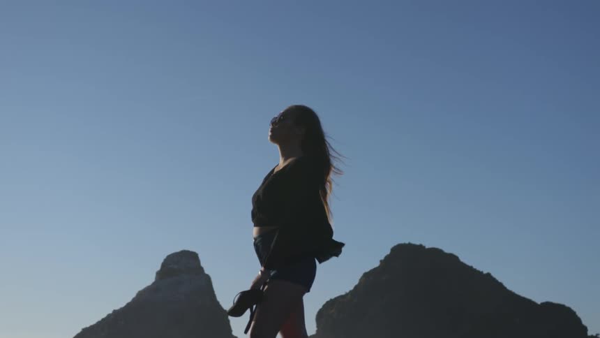 She standing in front on top of the mountain i think she is holding her shoes and a stick for blind people if shes holding a stick for one people shes not looking around if she isn't holding a stick for blind people then she's looking around