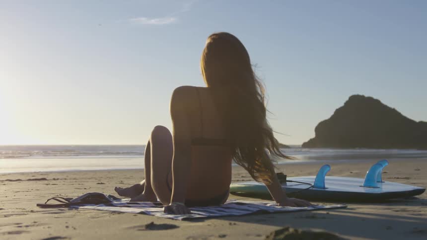 A woman sitting on a beach towel by the ocean