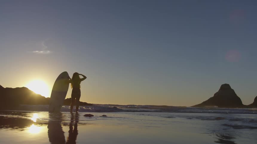 Woman holding a surfboard and looking to the horizon at the beach