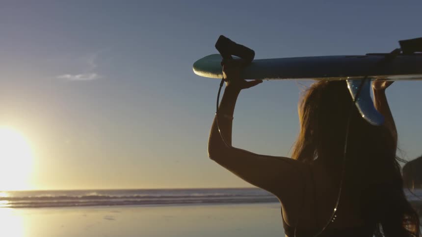 White woman holding a surfboard above her head at the beach
