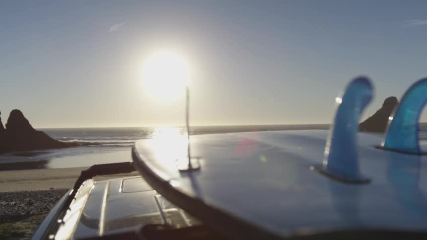 A surfboard that is on the top of a vehicle at the beach