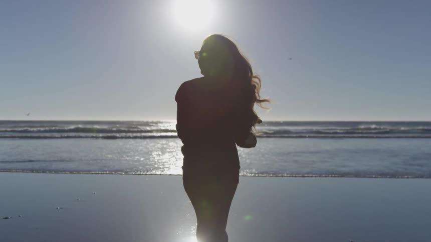Woman carries her sandals as she runs towards the ocean