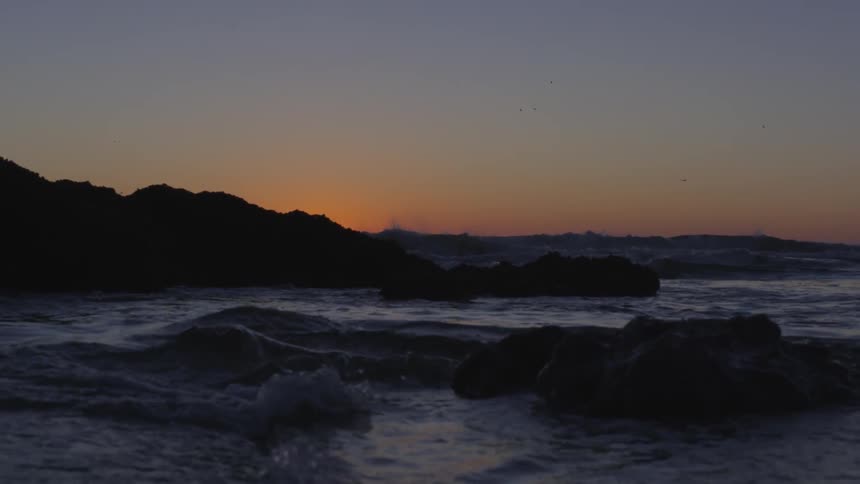 Ocean waves crash into a rocky shore at sunset