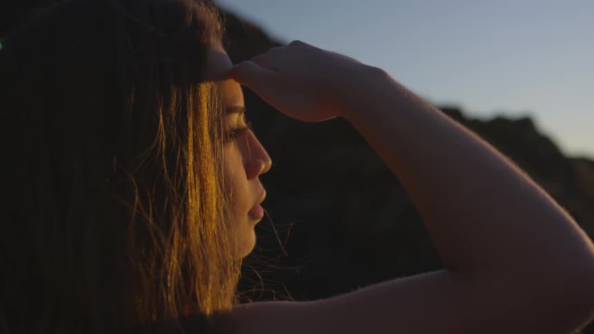 A woman looks off into the sunset shading her eyes with her hand
