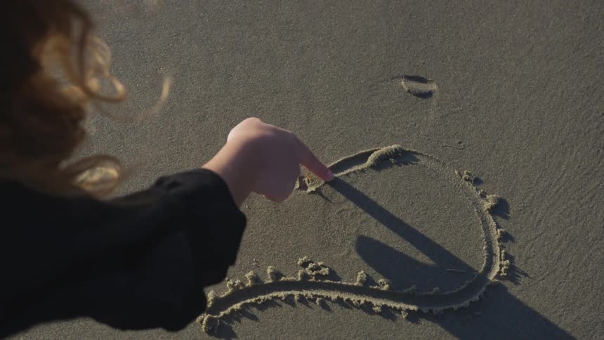 Woman draws a heart in the sand