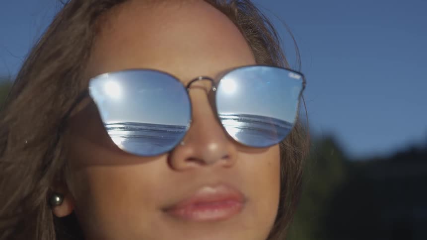 A woman wearing sunglasses looks out at the ocean at dusk