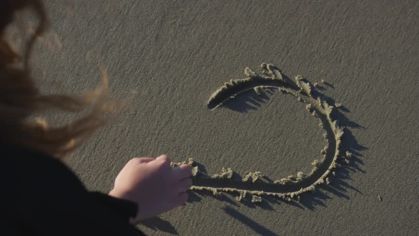 Woman drawing a heart on the sand with finger