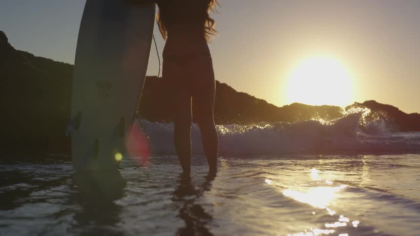 A surfer stands in the ocean watching the sun