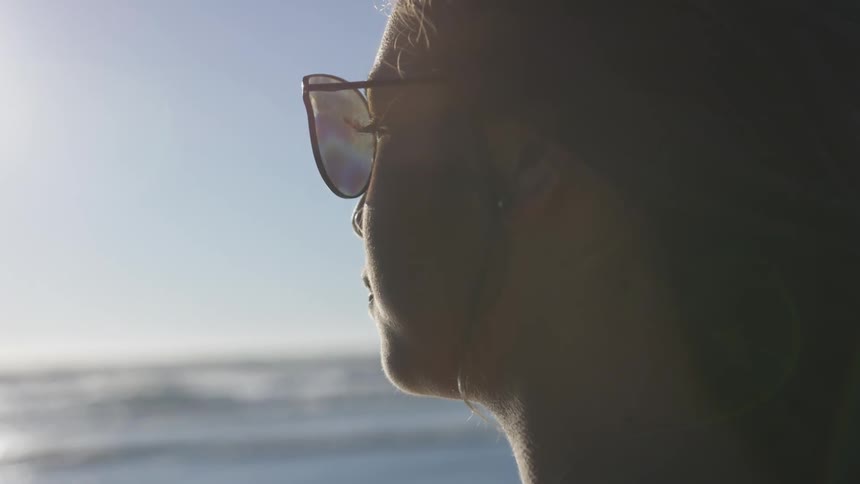 Woman wearing sunglasses stares out at ocean