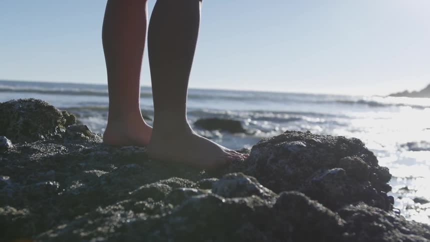 Persons low half standing on rocks by the sea