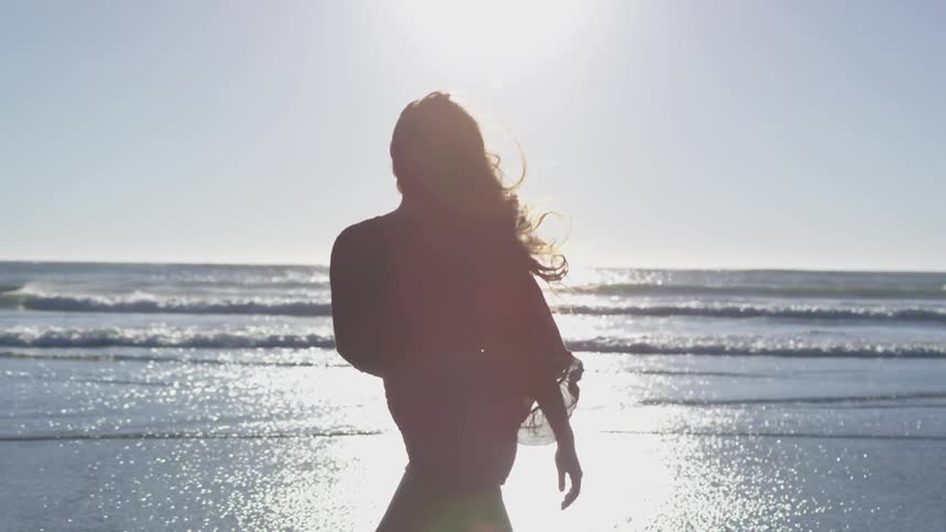 Woman walking on the shoreline of a beach at sunrise