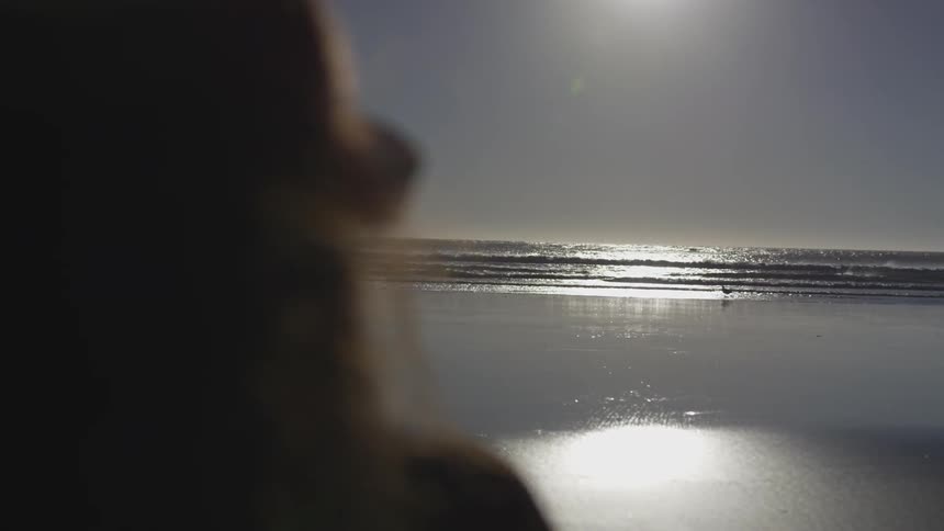 Woman standing on the shoreline of a beach watching at the horizon