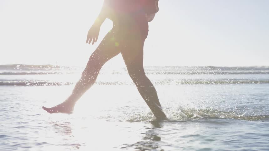 Woman walks along beach shore in bright sunlight