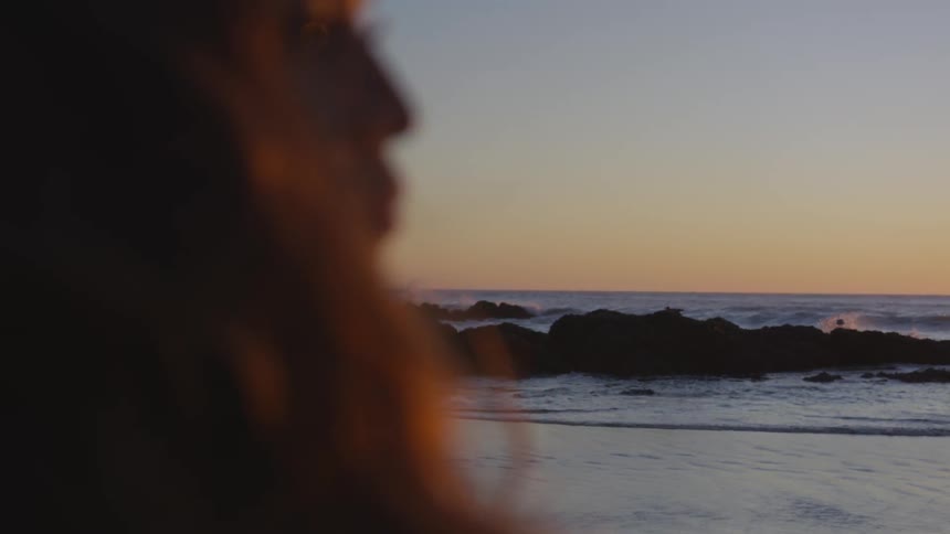 A woman on a beach stares into the distance